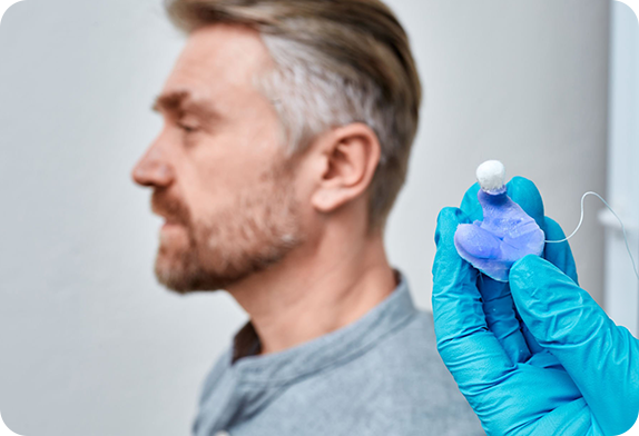 An audiologist in Perth holding custom moulded ear plugs, with a patient in the background